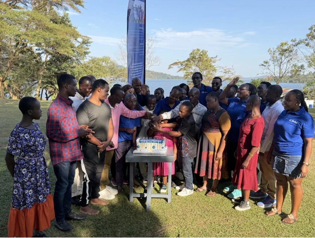 AMA Uganda team and community members gathered outdoors around a celebration cake